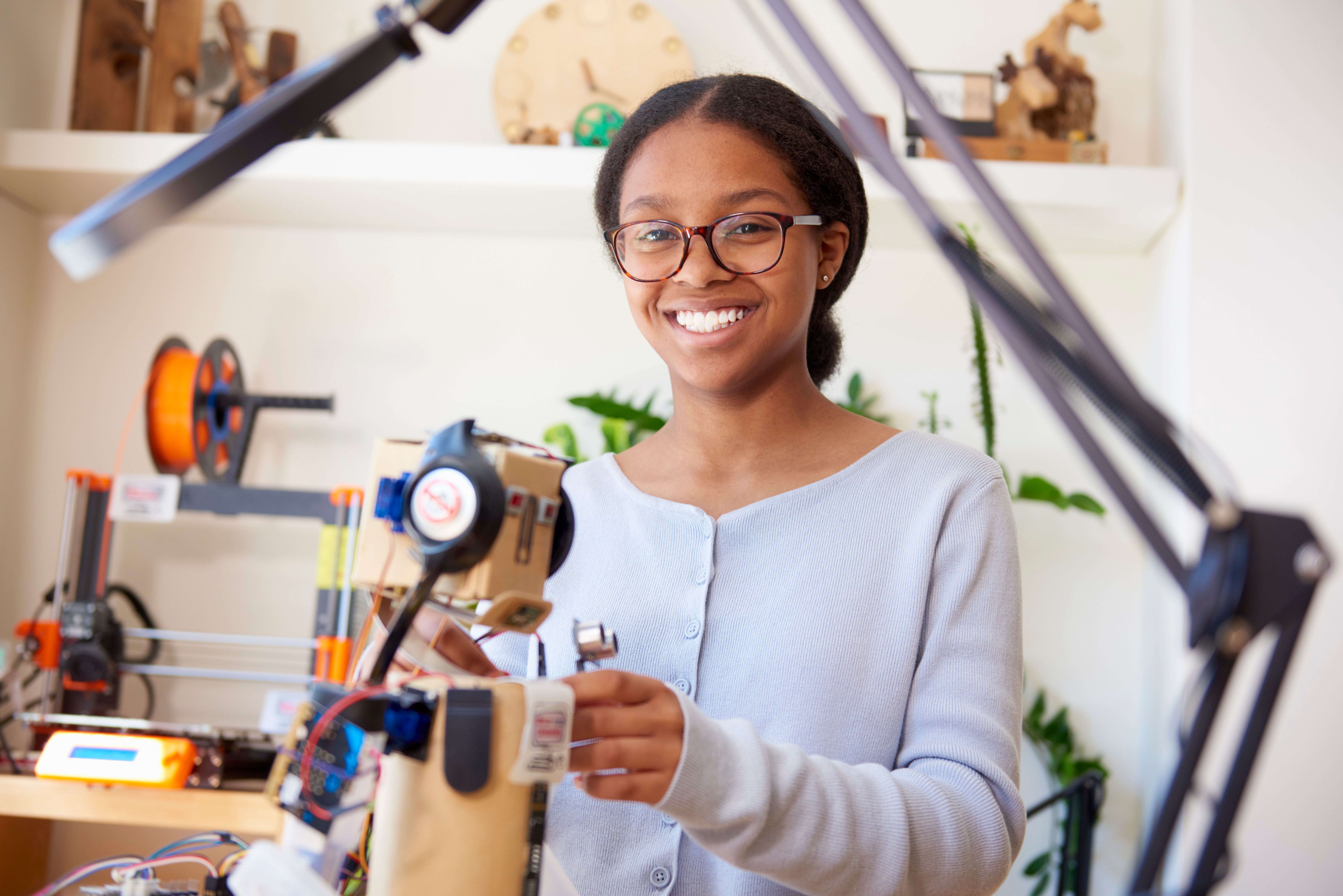 Smiling young woman in glasses works on an electronic device in a workshop.